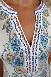 zoom in to the neckline of a woman wearing a short white dress with blue, green, yellow and red detailing/pattern, short sleeved