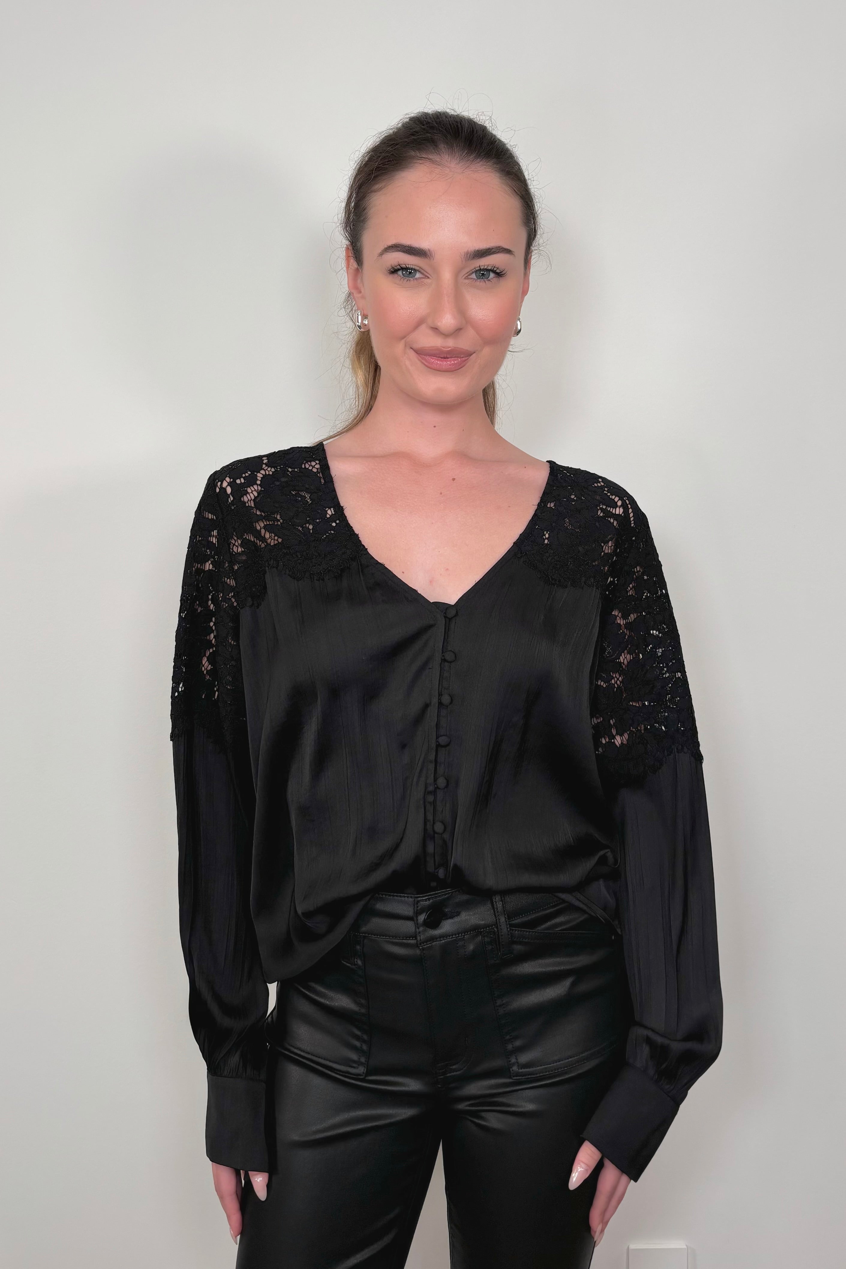 woman wearing a tucked black long sleeve satin blouse with lace detailing on the shoulders