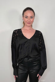 woman wearing a tucked black long sleeve satin blouse with lace detailing on the shoulders