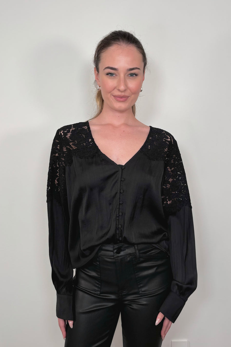 woman wearing a tucked black long sleeve satin blouse with lace detailing on the shoulders