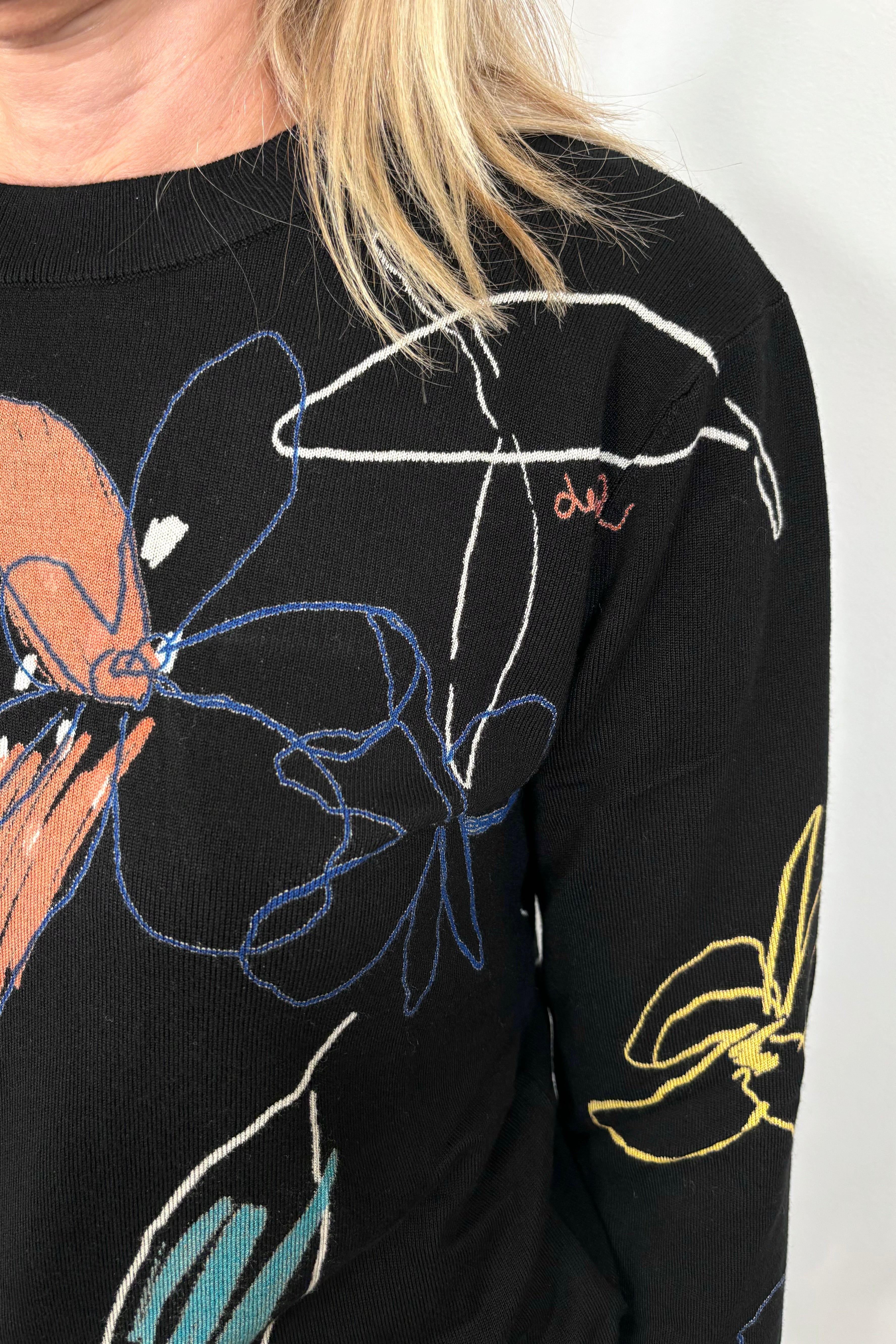 Front view shoulder zoom in of woman wearing a knit black top with all over coloured detailing