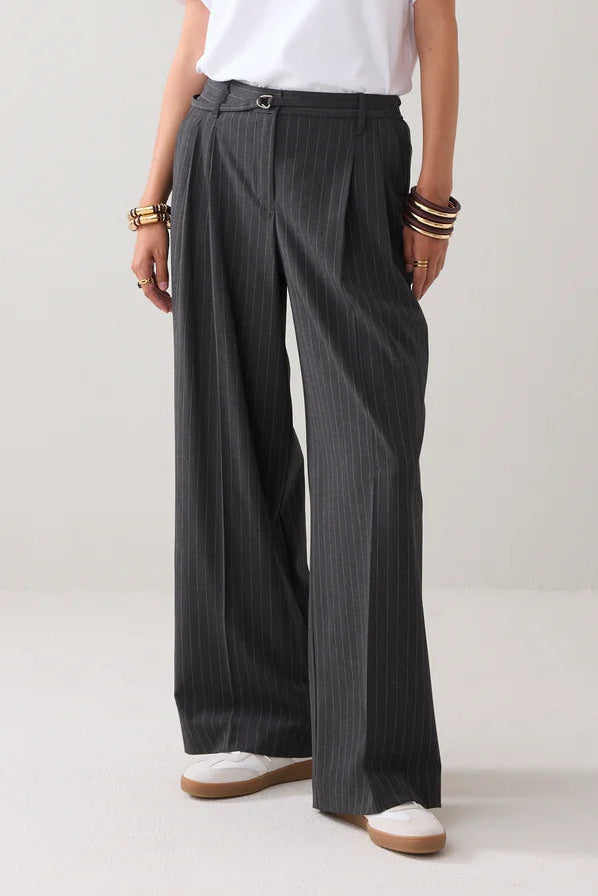 Woman wearing a white t-shirt and dark wide-leg pants on a plain background