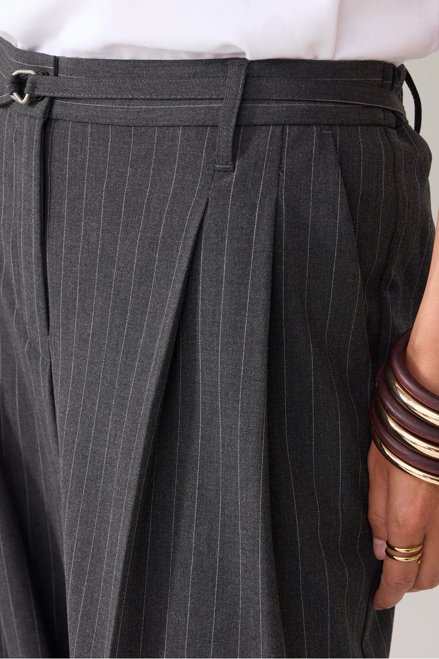 Gray pinstripe pants with a person wearing multiple bracelets on a neutral background