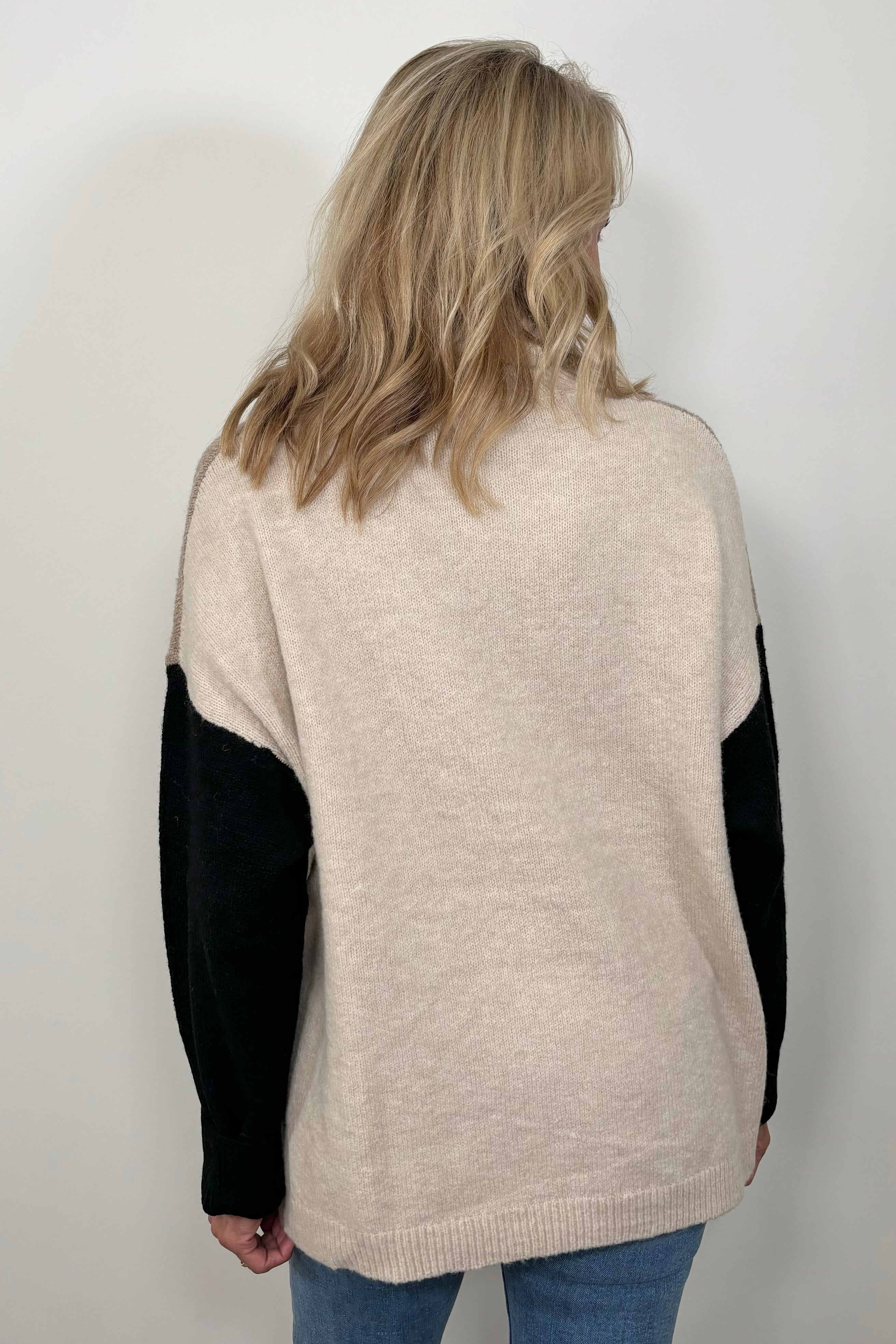 Back view of woman wearing a beige turtle neck sweater with black sleeves and oat meal coloured back