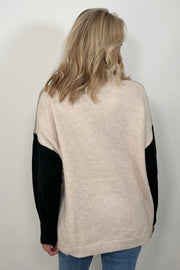 Back view of woman wearing a beige turtle neck sweater with black sleeves and oat meal coloured back