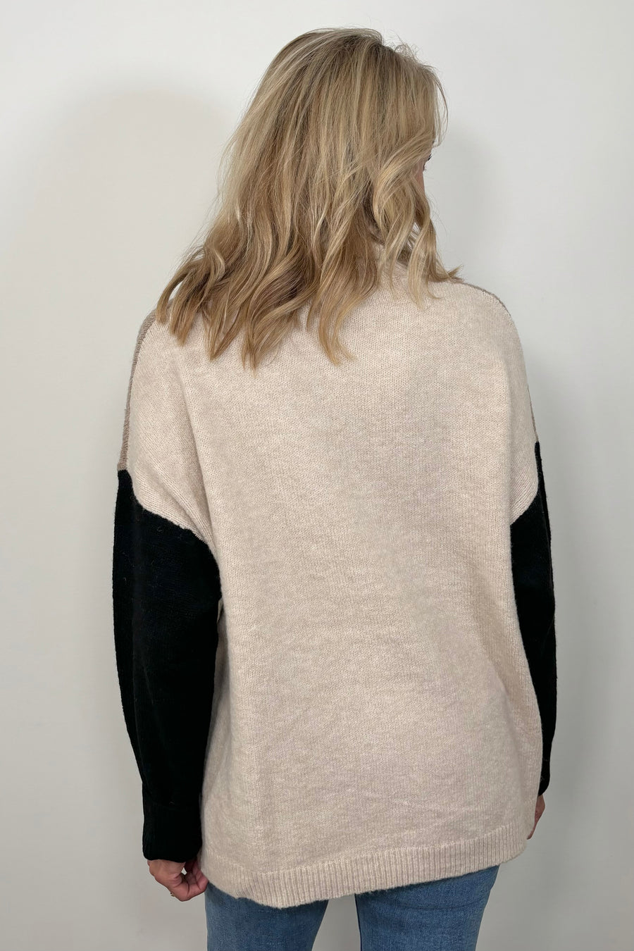 Back view of woman wearing a beige turtle neck sweater with black sleeves and oat meal coloured back