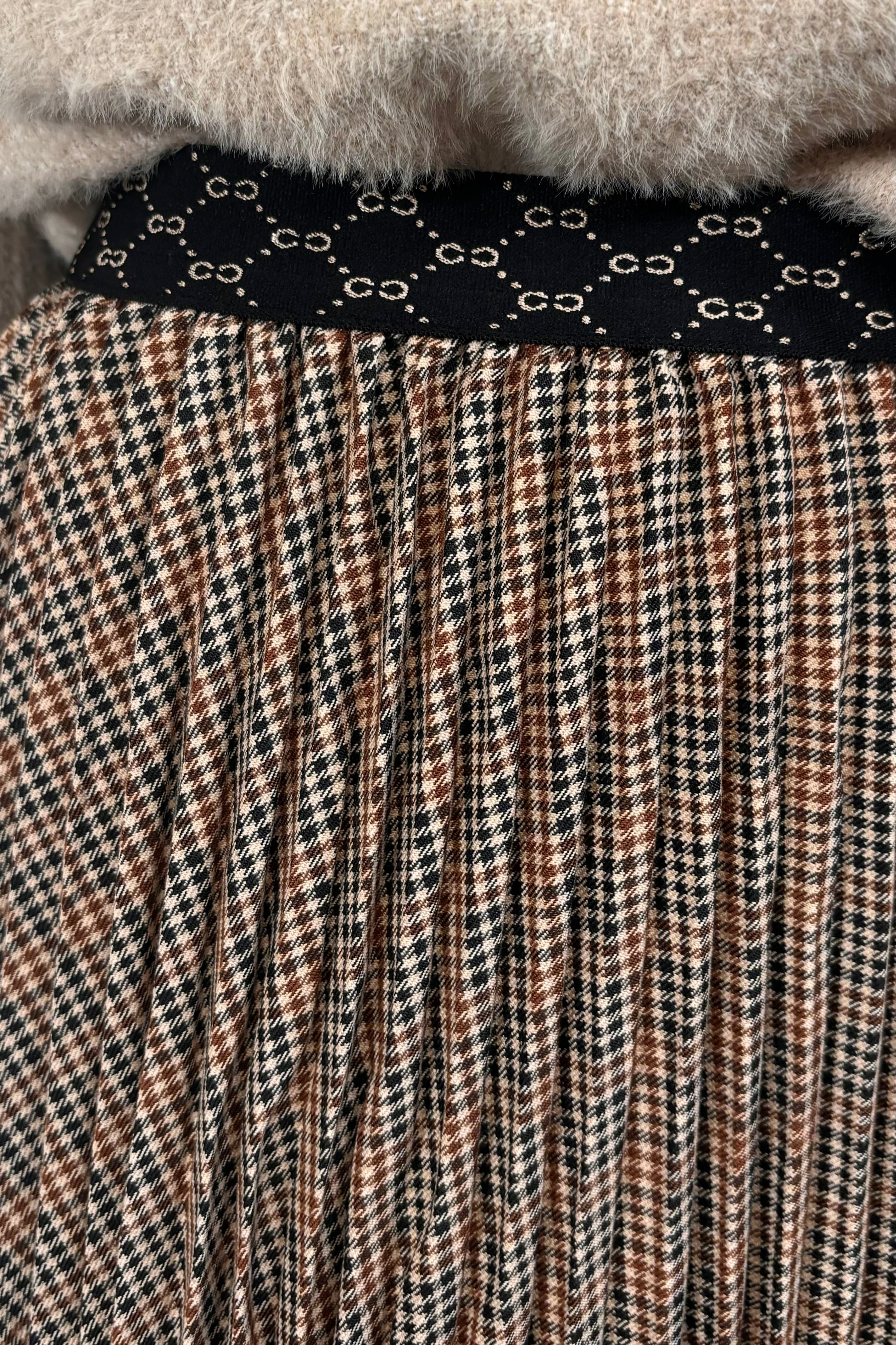 Person wearing a beige sweater and plaid skirt on a light background