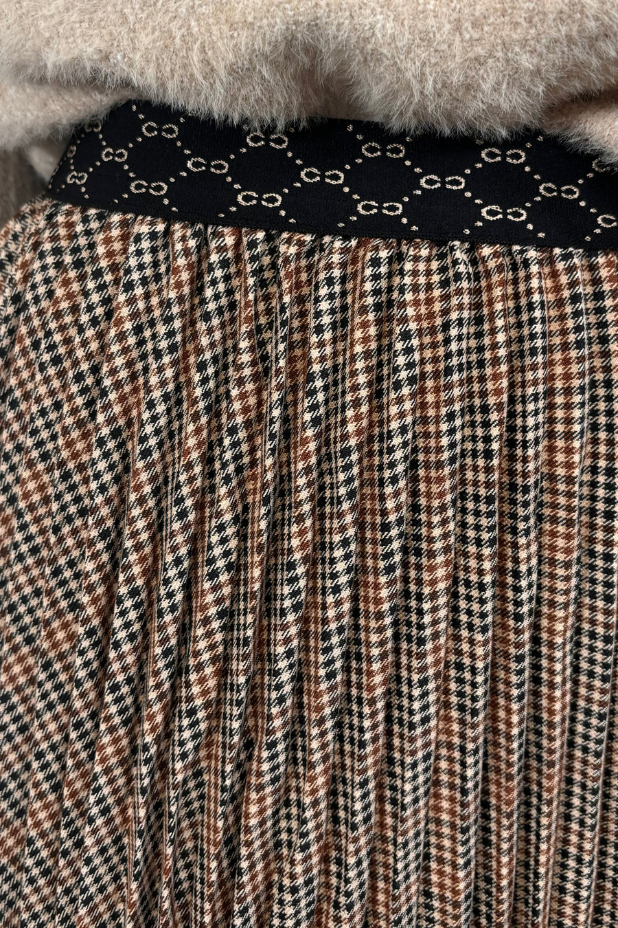 Person wearing a beige sweater and plaid skirt on a light background