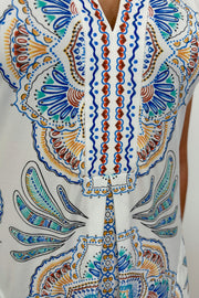 Zoom in of a woman’s torso wearing a short white dress with blue, green, yellow and red detailing/pattern, short sleeved