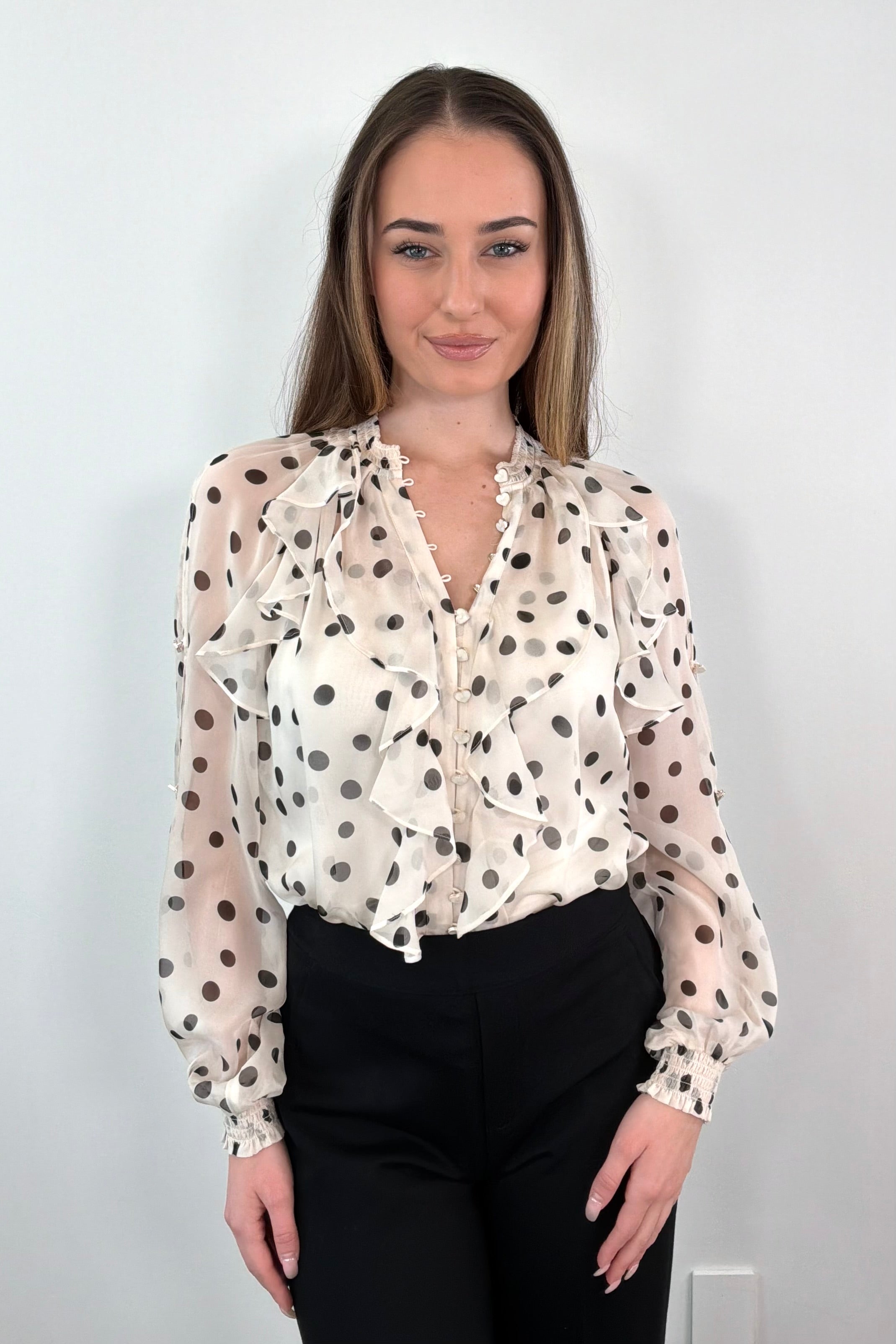 Woman wearing a sheer ruffle blouse with polka dots tucked in