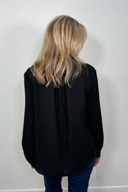 Back view of a woman wearing a black blouse with ruffles and blue jeans 