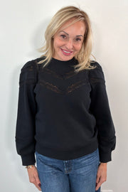 woman wearing a black sweatshirt with lace detailing and cuffed poplin  sleeves