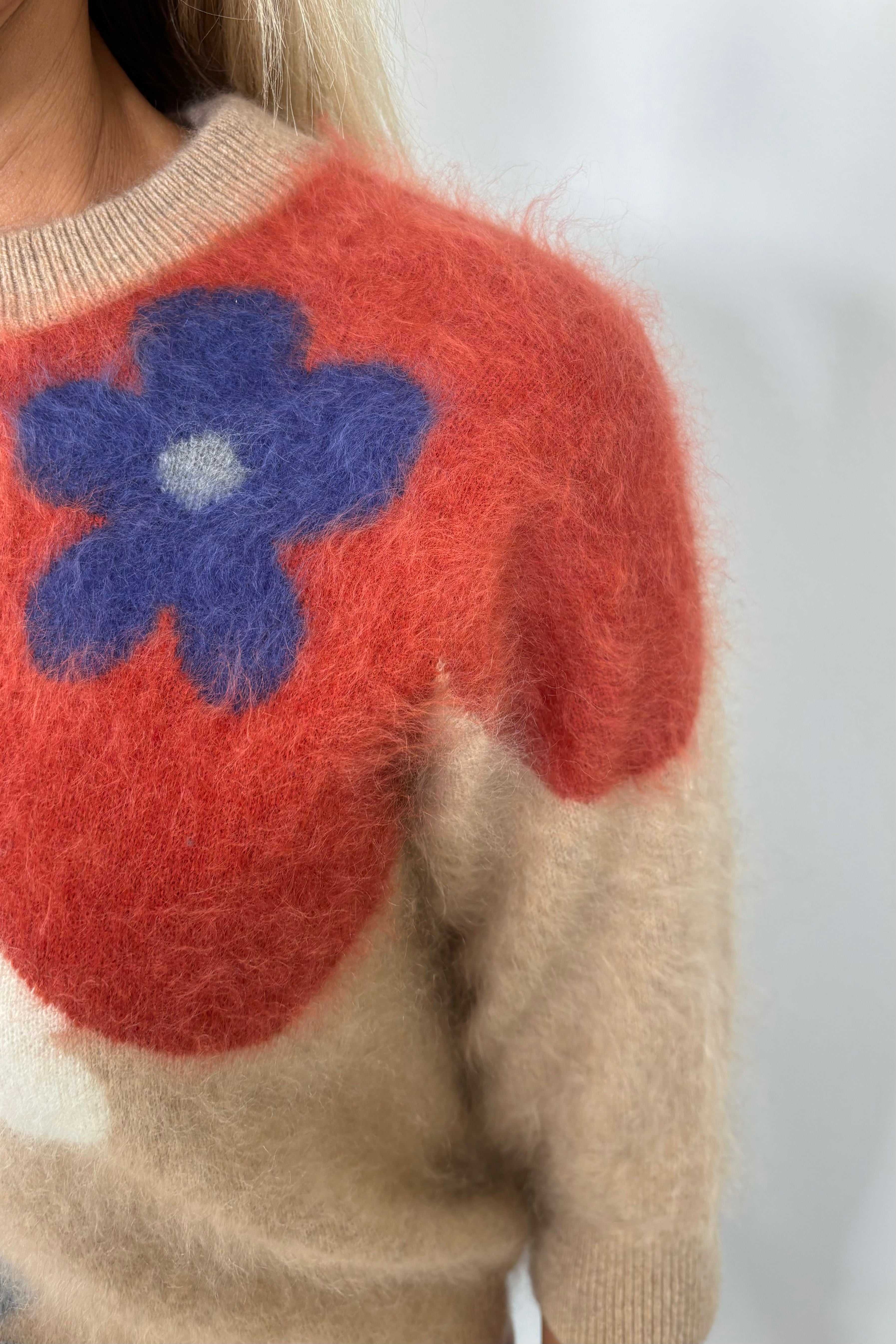 Zoom in of the left shoulder of a woman wearing a tan 100% brushed cashmere sweater with a flower pattern 