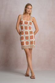 full body of a woman wearing an orange, white and beige patterned crochet short dress 