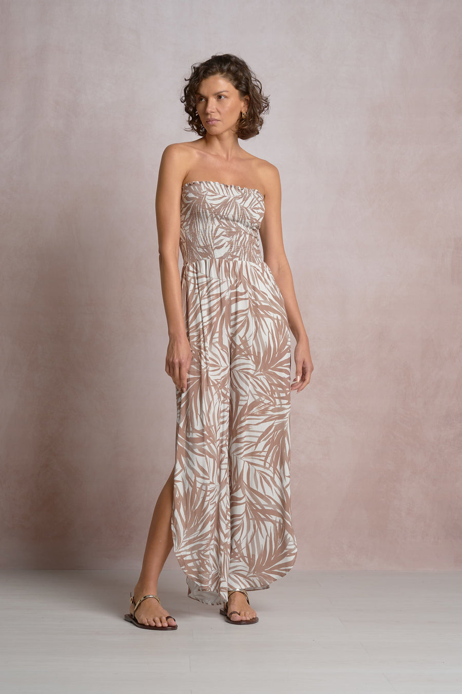 Woman wearing a beige and white strapless dress with a  palm leaf pattern 