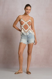woman wearing a white, beige, orange and brown crochet frayed tank top with blue shorts