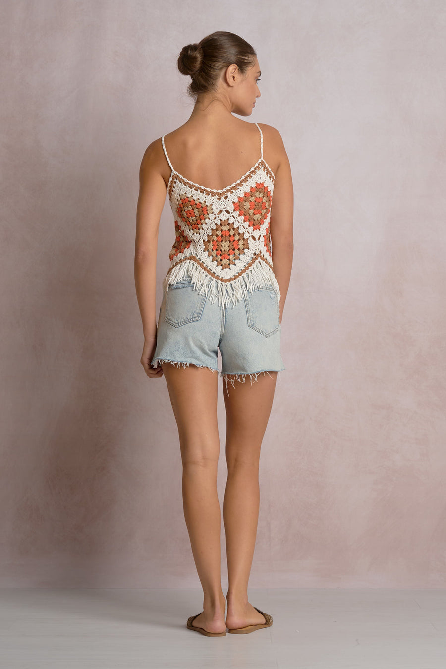 woman wearing a white, beige, orange and brown crochet frayed tank top with blue shorts