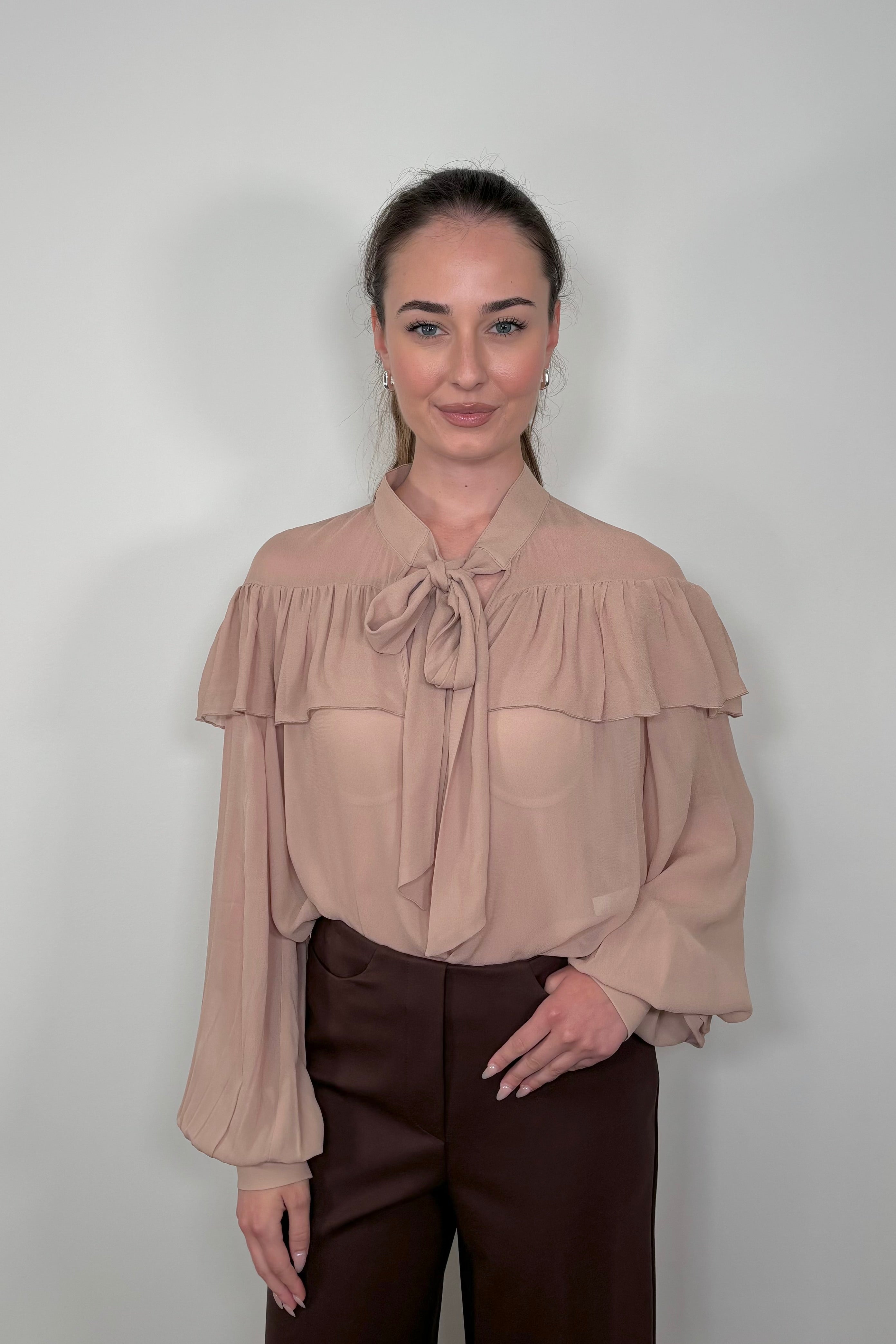Front view of woman wearing a nude coloured sheer ruffle tie neck blouse