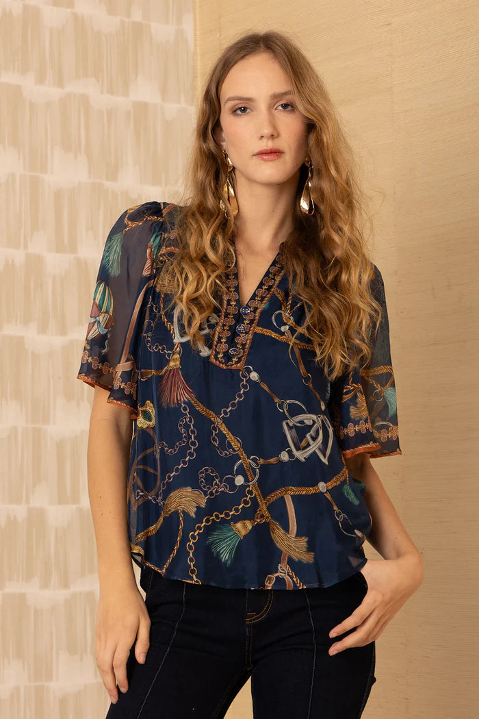 Woman wearing a navy patterned silk blouse against a beige wall
