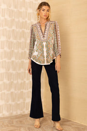  Full body view of a woman wearing patterned v-neck top with intricate and colourful designs.
