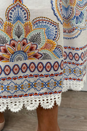 Zoom into the hemline of a woman wearing white sleeveless midi dress with a blue, red and orange pattern as well as crochet detailing