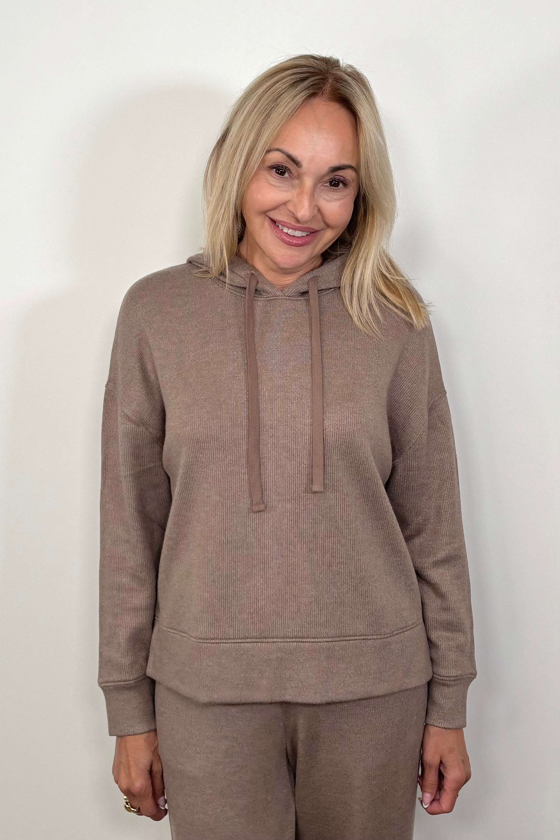 Front view of a woman wearing a matching set of light brown hoodie and pants on a white background