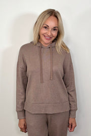 Front view of a woman wearing a matching set of light brown hoodie and pants on a white background