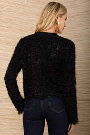 Person wearing a black textured sweater and dark jeans against a wooden wall.