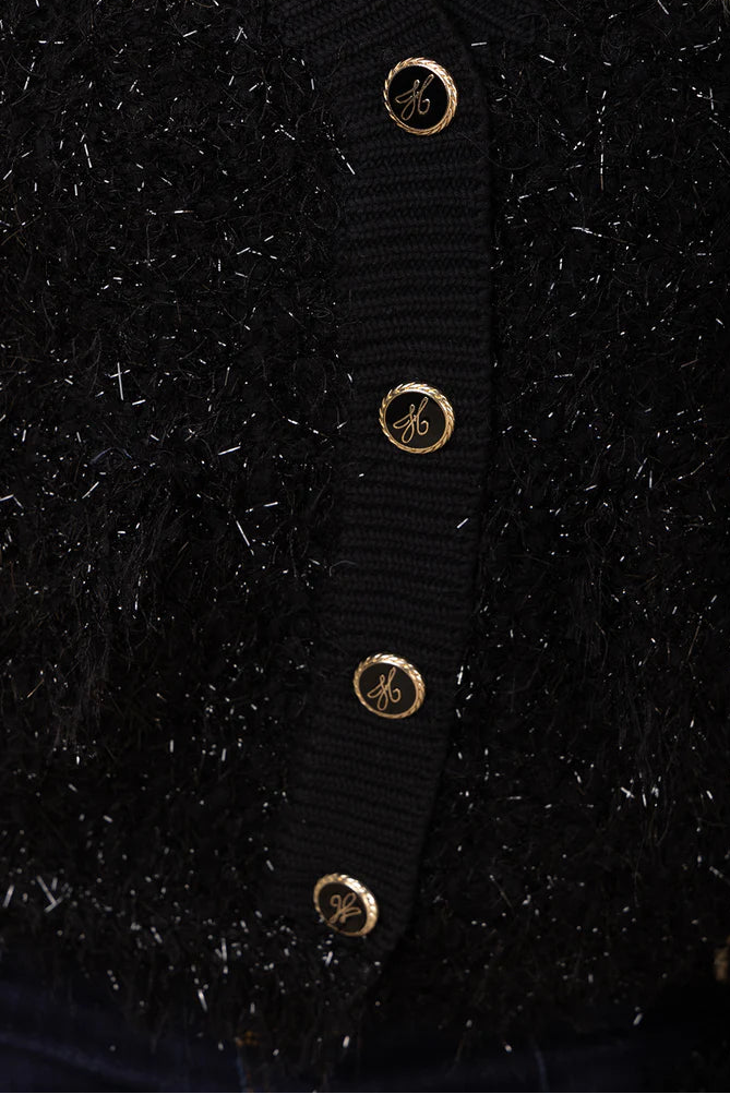 Close-up of a black cardigan with gold buttons on a dark background