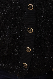 Close-up of a black cardigan with gold buttons on a dark background