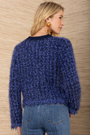Woman wearing a blue textured sweater and jeans against a wooden background