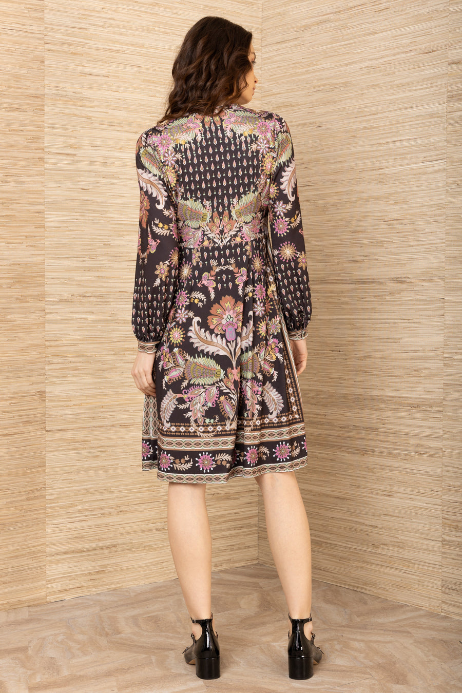 Woman wearing a patterned dress standing against a textured beige wall.