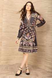 Woman wearing a patterned dress standing against a wooden paneled wall.