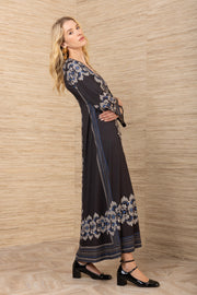 Woman wearing a long, dark dress with white floral patterns against a wooden wall.