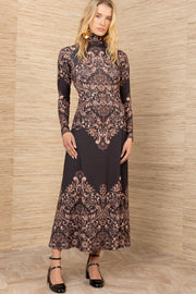 Woman wearing a long, patterned dress against a wooden paneled wall.