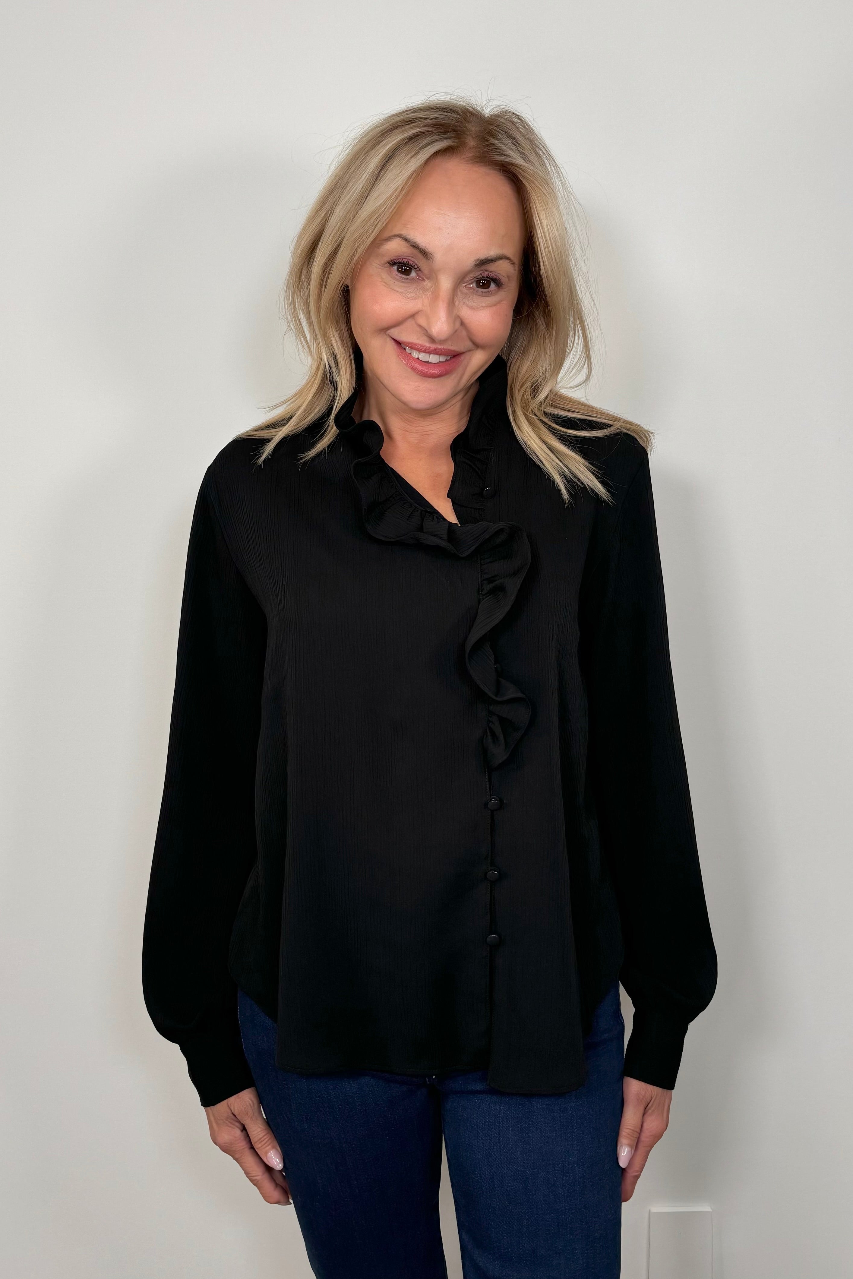 Front view of a woman wearing a black blouse with ruffles and blue jeans 