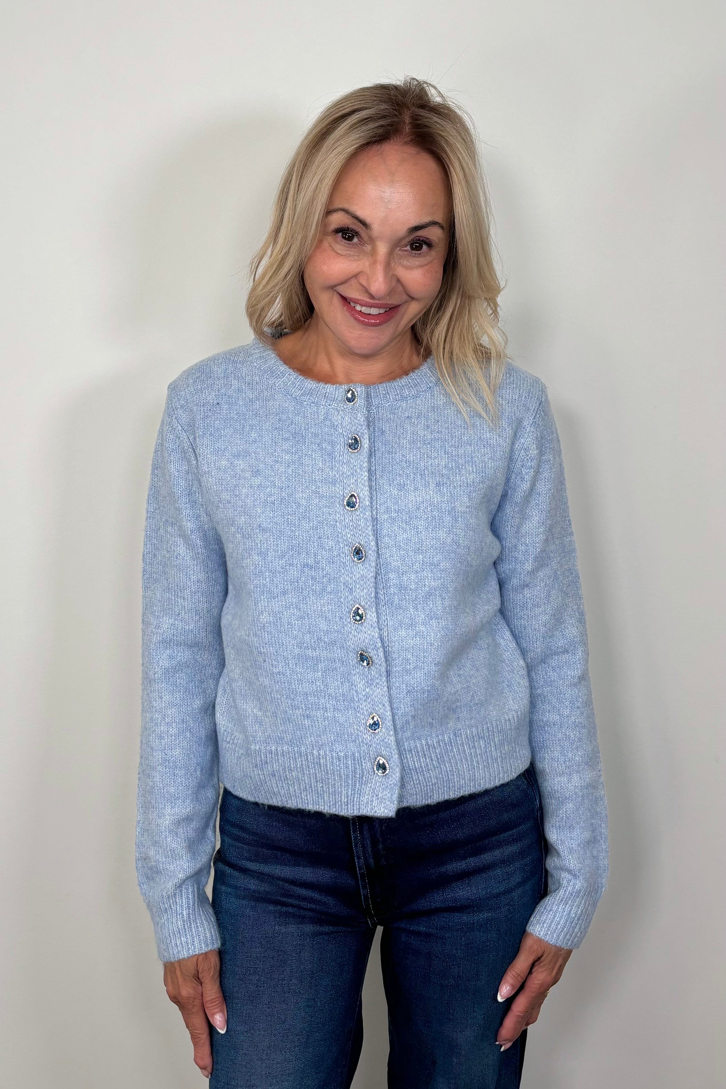 Front view of woman wearing a blue cardigan with gemstones as buttons done up