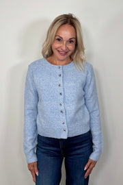 Front view of woman wearing a blue cardigan with gemstones as buttons done up