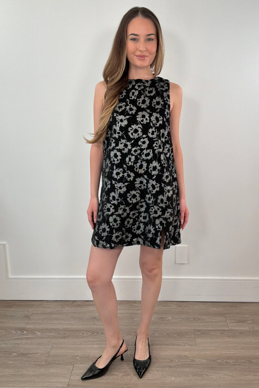 Woman wearing a black floral dress against a white wall.