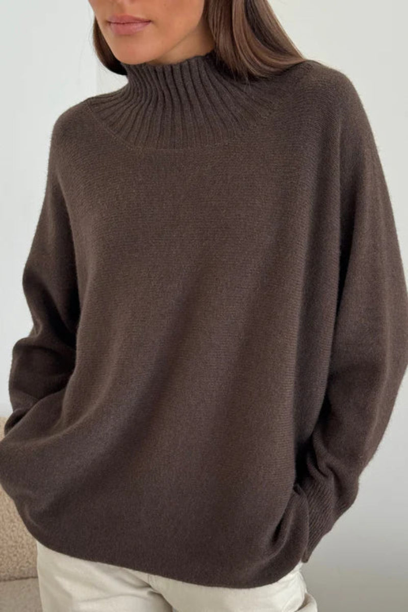 Person wearing a brown sweater and light-colored pants against a neutral background