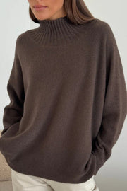 Person wearing a brown sweater and light-colored pants against a neutral background