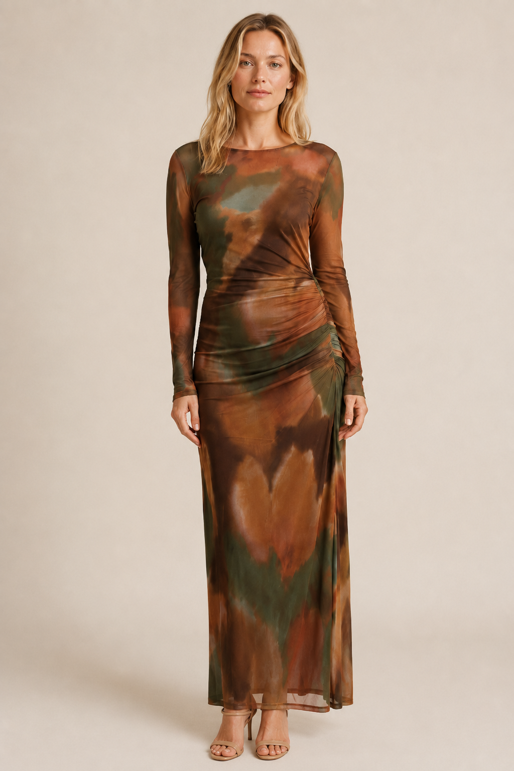 A woman modeling a long-sleeve maxi dress with an abstract tie-dye pattern in earthy brown, green, and orange tones. 