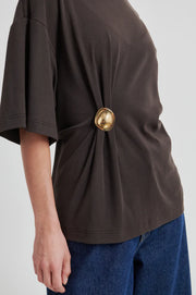Woman wearing a brown short-sleeve crewneck top with a side ring detail, side