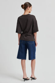 Woman wearing a brown short-sleeve crewneck top with a side ring detail, back