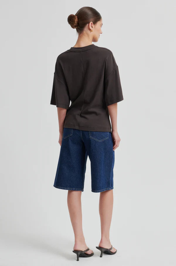 Woman wearing a brown short-sleeve crewneck top with a side ring detail, back
