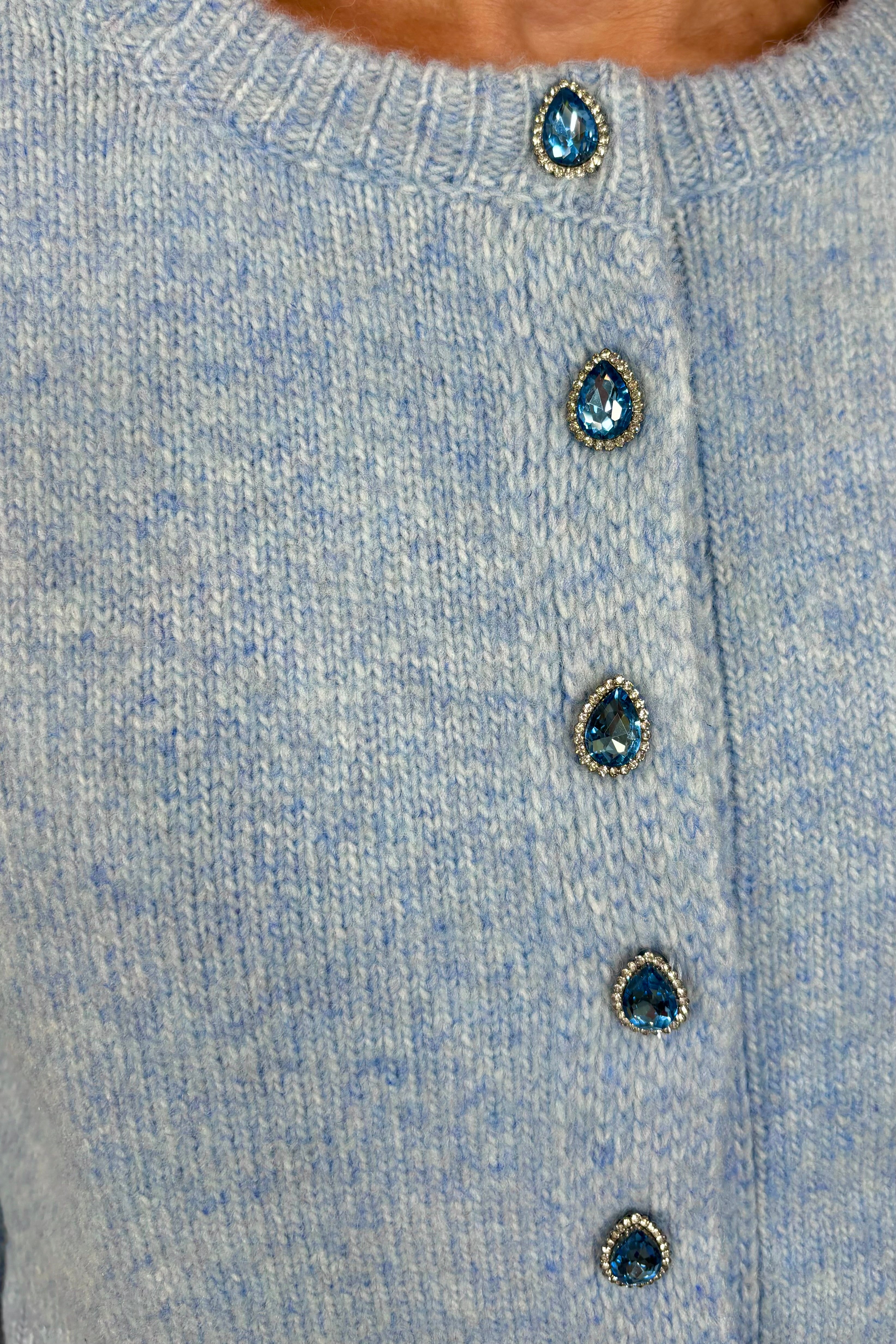 Zoom in view of woman wearing a blue cardigan with gemstones as buttons done up