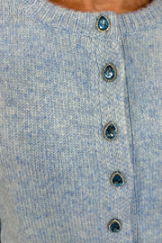 Zoom in view of woman wearing a blue cardigan with gemstones as buttons done up
