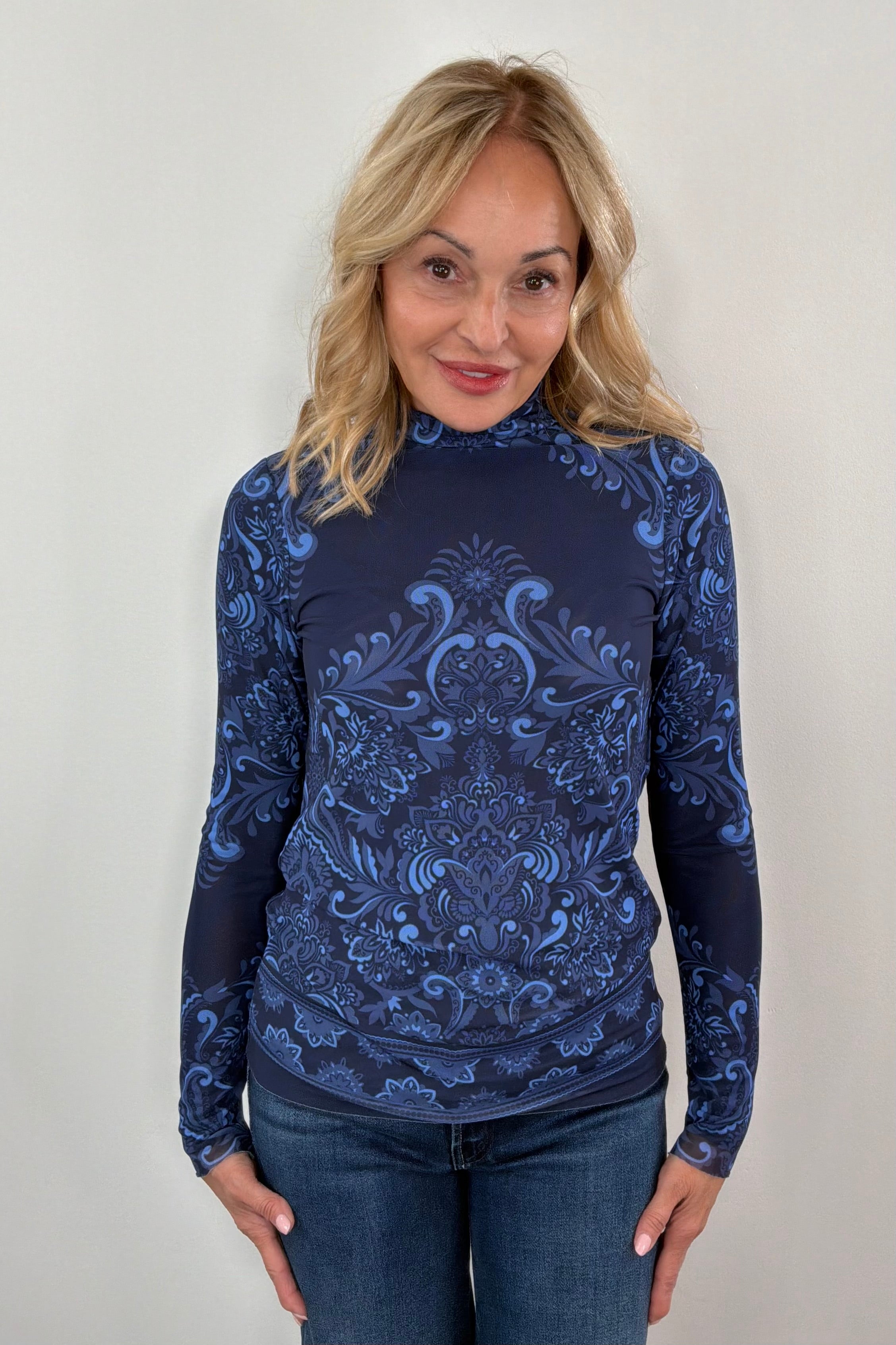 Woman wearing a blue patterned long-sleeve mesh top against a plain background