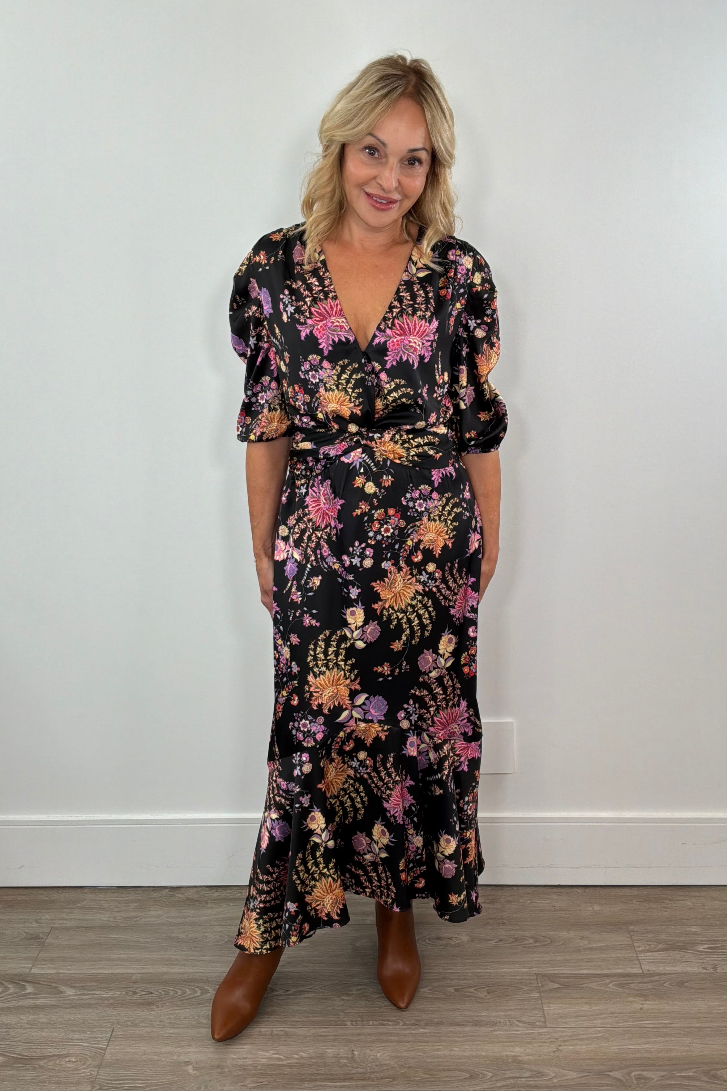 Woman wearing a floral black dress standing against a white wall.