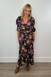 Woman wearing a floral black dress standing against a white wall.